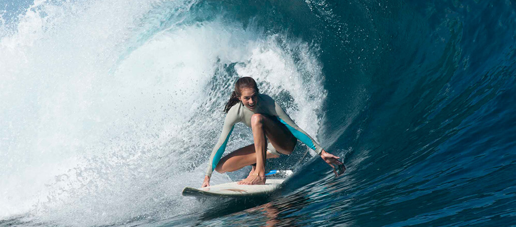Surfer crouching low while riding inside a powerful blue wave.