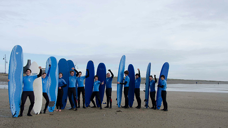 Birthday group in wetsuits holding surfboards and posing together on the beach.