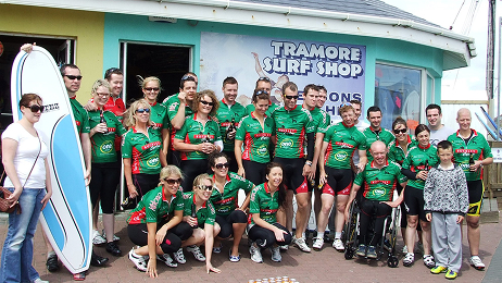 Corporate group posing outside Tramore Surf Shop, some holding surfboards and wearing team jerseys.