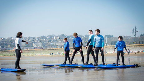 Surf instructor teaching a group of students standing on boards on the sand during a private lesson.