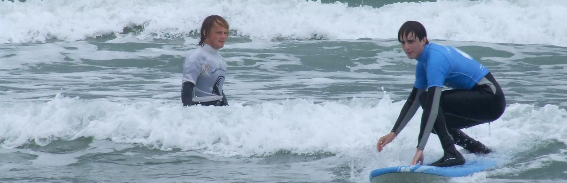 Surf instructor guiding a student riding a small wave during a private beginner surf lesson.