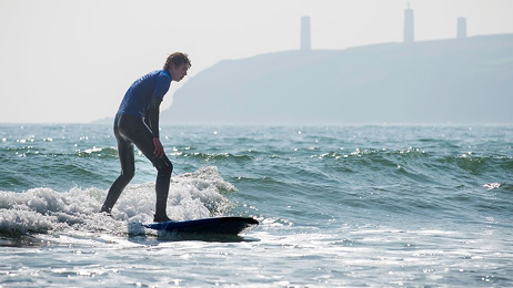 Surfer riding a small wave on a surfboard near the shore during a lesson.