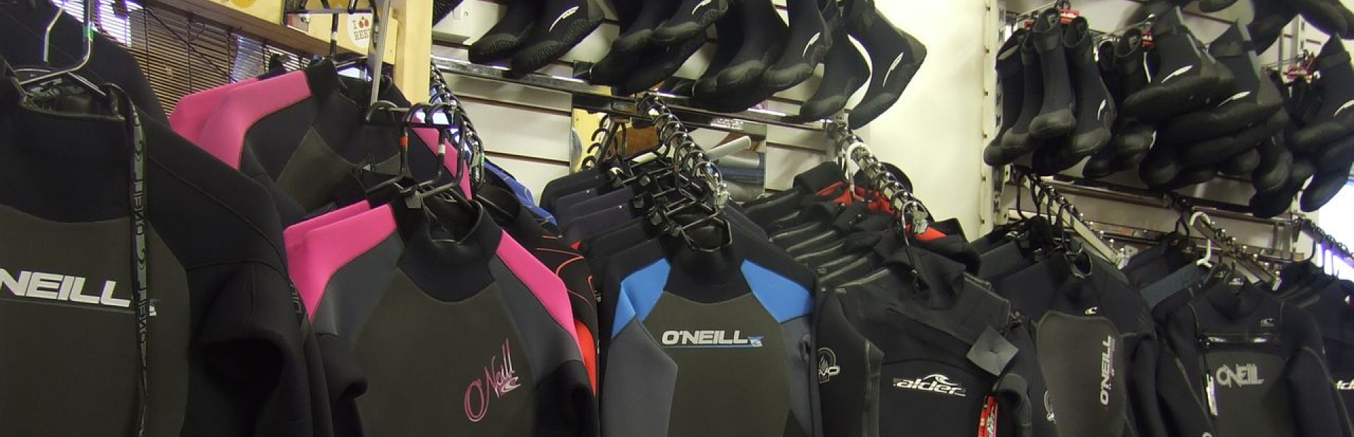 Display of wetsuits and diving gear hanging on racks inside a water sports rental shop.
