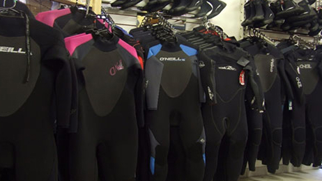 Row of wetsuits hanging on racks inside a surf equipment rental shop.
