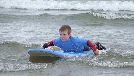 Young child paddling on a surfboard in shallow waves during a surf camp.