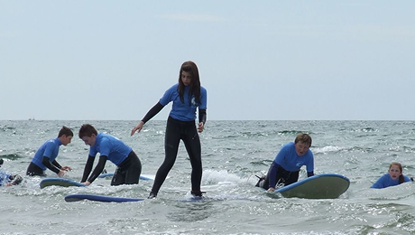 Group of children learning to surf in shallow water with an instructor during a surf camp.