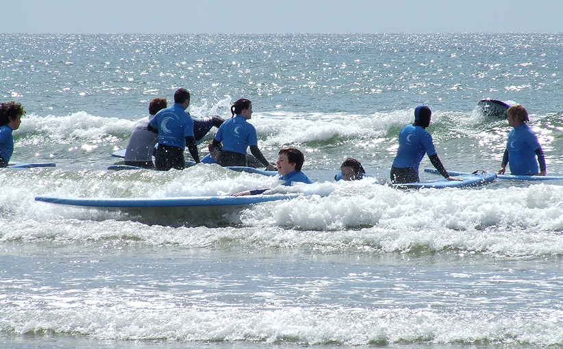 Group of young surfers practising on surfboards in shallow waves, with an instructor nearby.