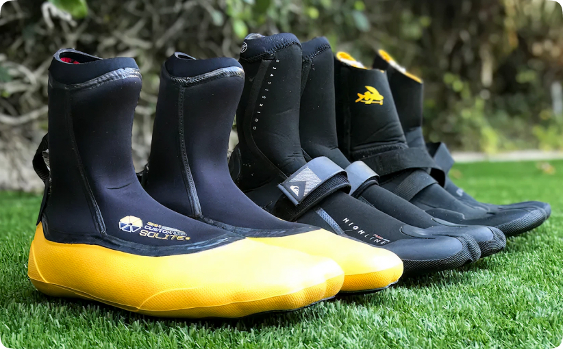 Neoprene water sports boots lined up on grass, including yellow-soled and black surf booties.