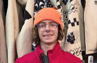Portrait of a surf shop staff member wearing an orange beanie and red jacket indoors.