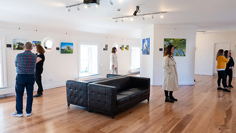 Coastguard Cultural Centre Tramore visitors viewing artwork displayed on the walls inside a bright gallery space with wooden floors and a black sofa.