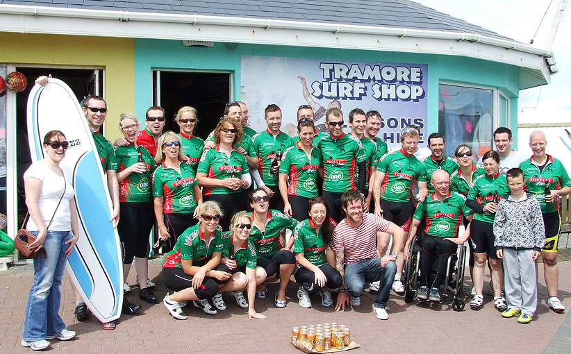 Corporate group posing outside Tramore Surf Shop, some holding surfboards and wearing team jerseys.