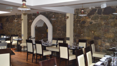 Crew’s Steak and Seafood Restaurant dining area with stone walls, arched doorway feature, and tables set with white chairs and glassware.