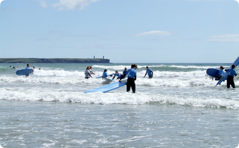 Group of surfers carrying boards and entering the water during a family surf lesson.