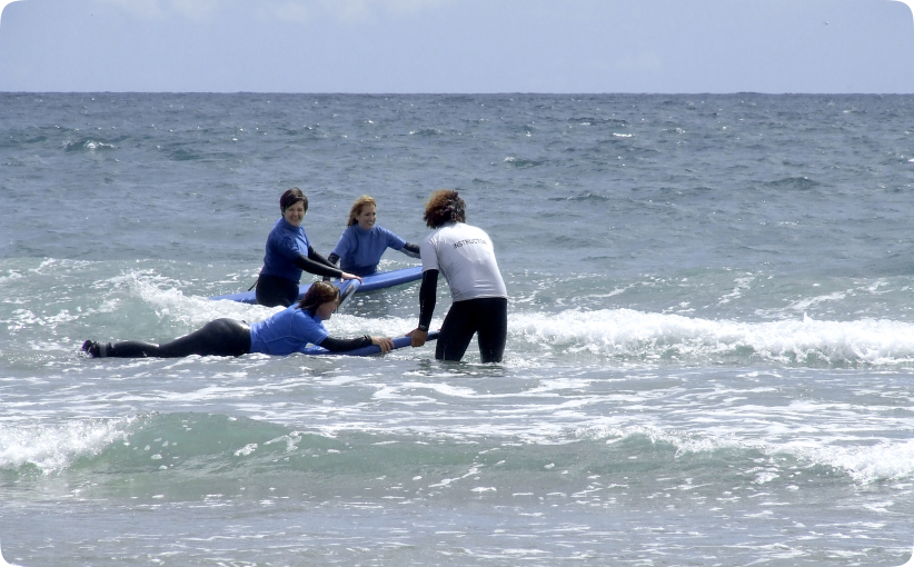 Surf instructor assisting two students on a board in shallow water during a family lesson.