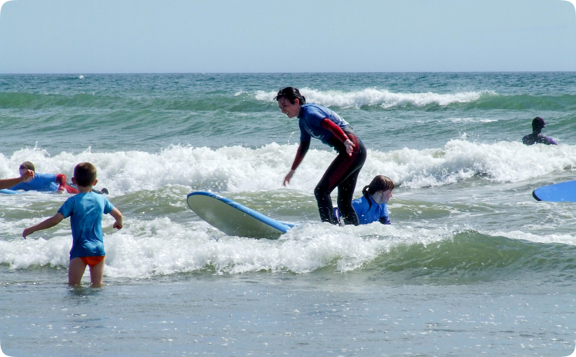 Adult surfing a small wave while children practice nearby during a surf lesson.