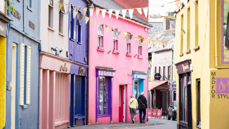 Colourful shopfronts lining a narrow street in Cork, with two people walking along the pavement.
