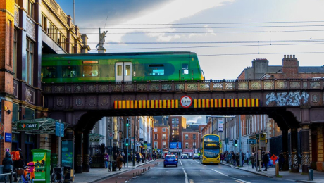 Dublin train crossing an iron railway bridge above a city street with traffic and pedestrians below.