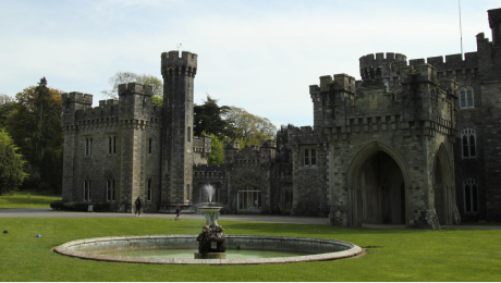 Wexford castle with round towers and an arched entrance, set behind a lawn with a circular fountain in the foreground.