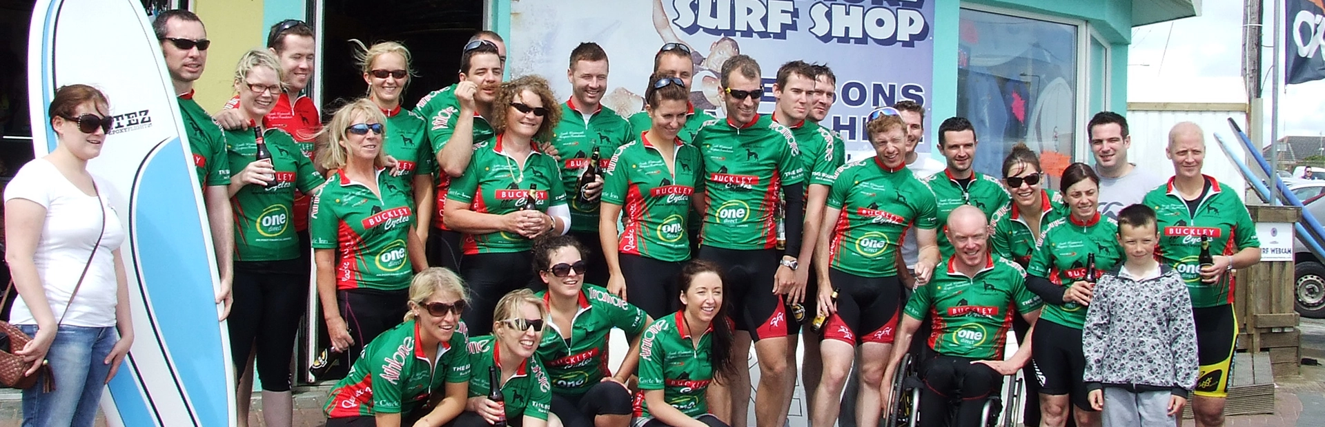Corporate group posing outside Tramore Surf Shop, some holding surfboards and wearing team jerseys.
