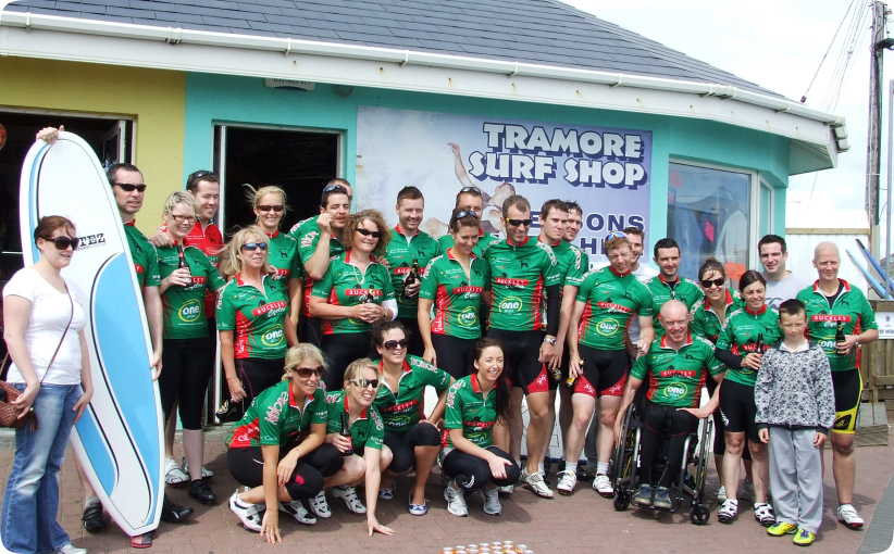 Corporate group in matching jerseys posing outside Tramore Surf Shop with a surfboard.