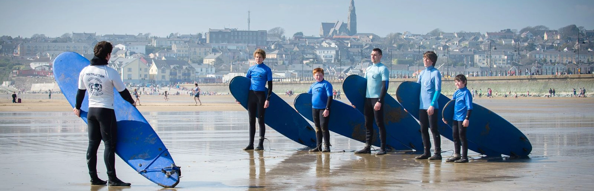 Surf instructor giving instructions to a line of students holding surfboards on the beach.