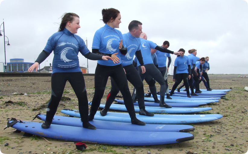 Group of surfers practicing balance on boards on the sand during a beginner lesson.