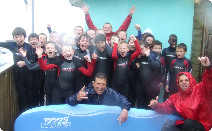 Group of children in wetsuits cheering together with instructors after a surf lesson.