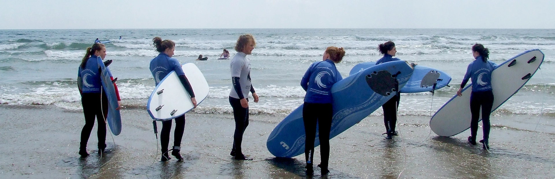 Group of surfers carrying boards into the water at the start of a lesson.