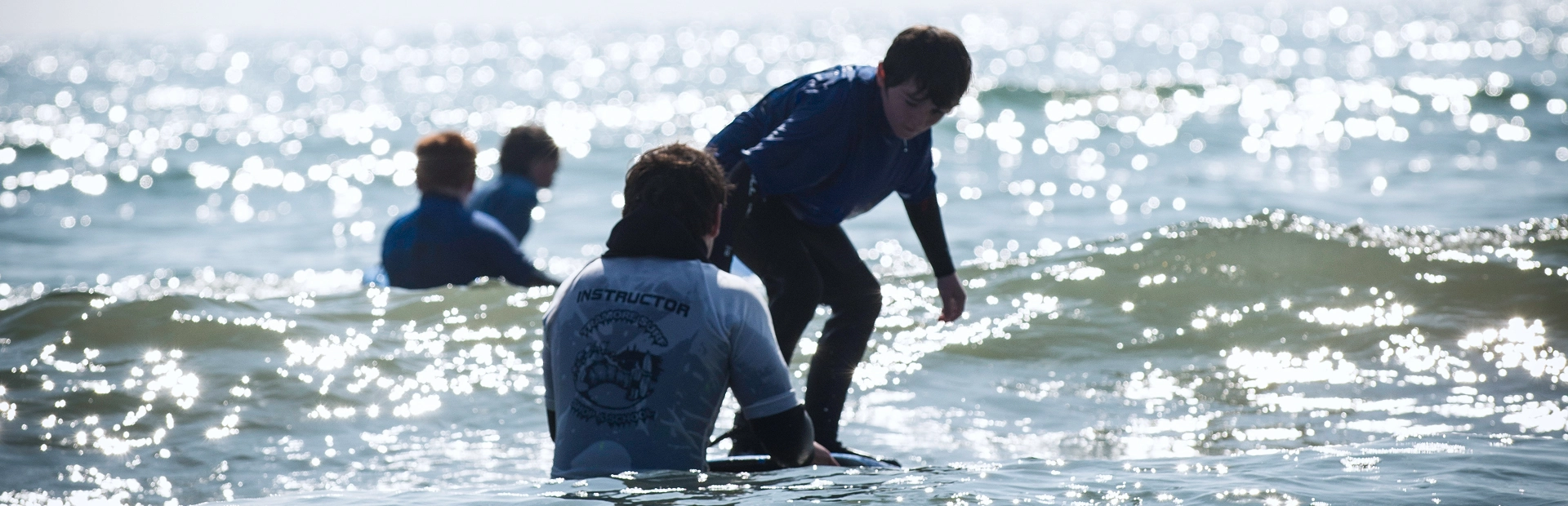 Child surfing a small wave while an instructor supports from the water during a lesson.