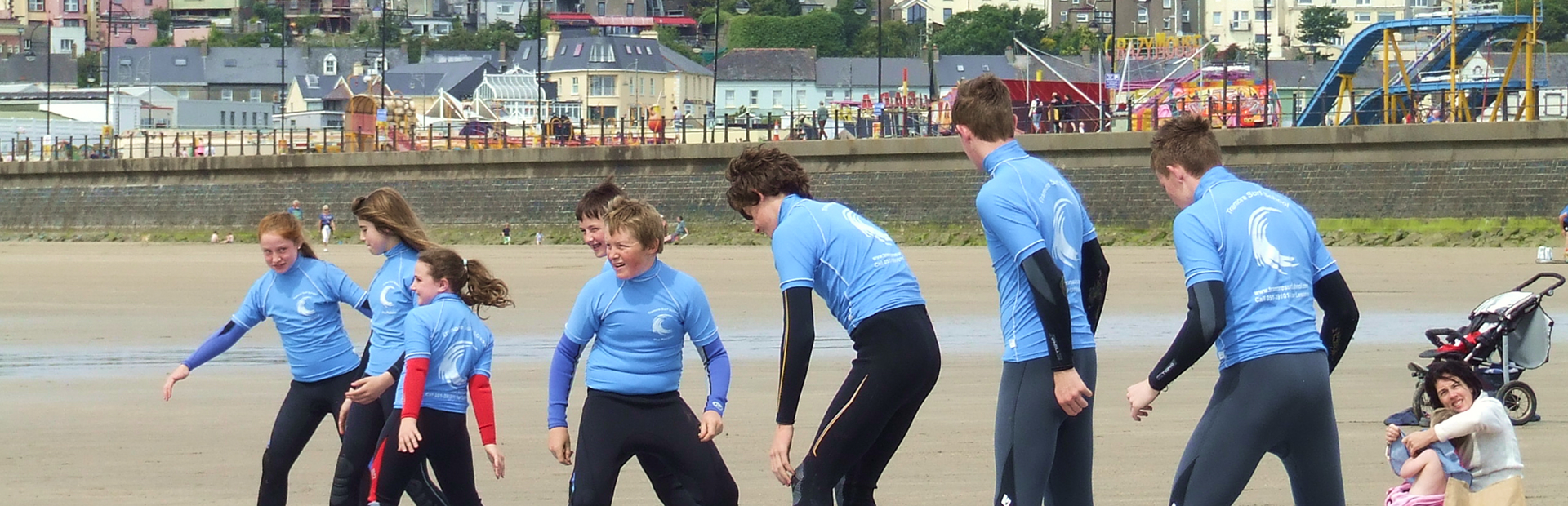 Group of children in wetsuits warming up on the beach before a public surf lesson.
