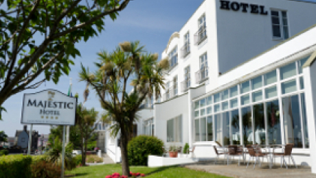 White hotel building with palm trees, outdoor seating, and a sign reading Majestic Hotel.