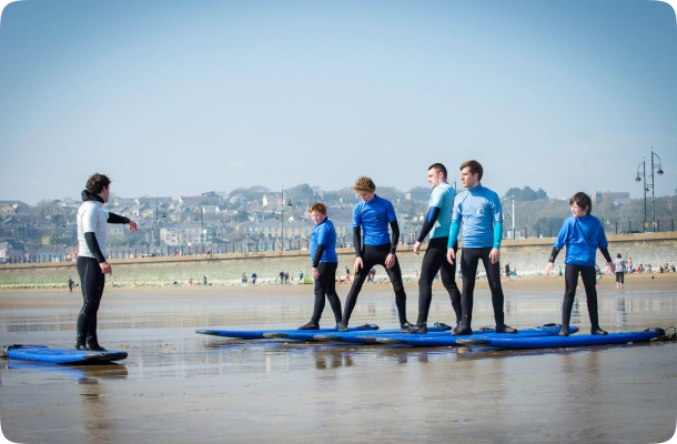 Surf instructor coaching a small group standing on boards on the sand during a beginner lesson.