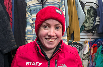 Portrait of a smiling surf shop staff member wearing a red beanie and staff jacket indoors.