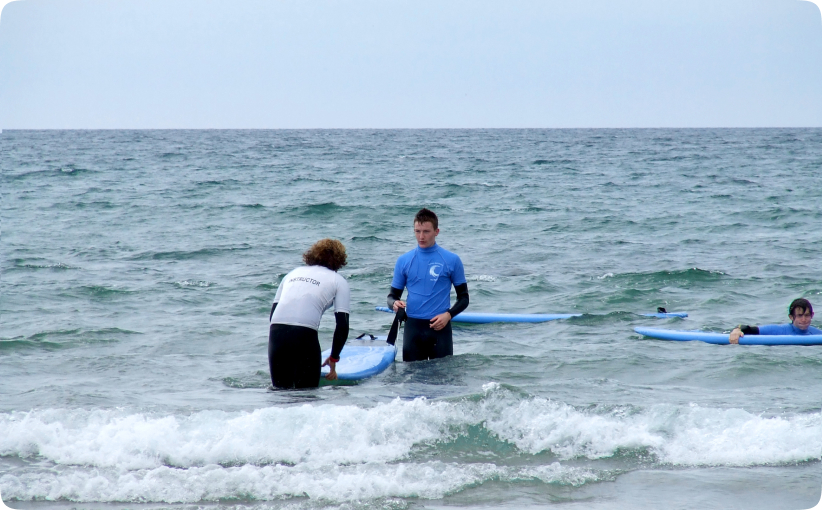 Surf instructor helping a student position a board in shallow water during a private lesson.