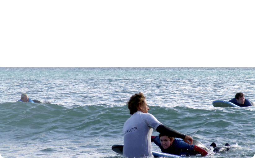 Surf instructor assisting a student on a board in the water during a private lesson.