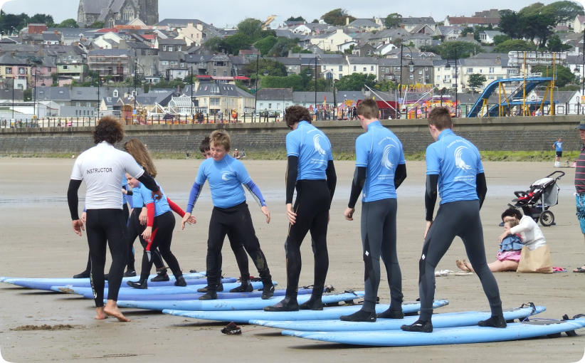 Instructor helping young surfers practice standing on boards on the sand during a beach lesson.