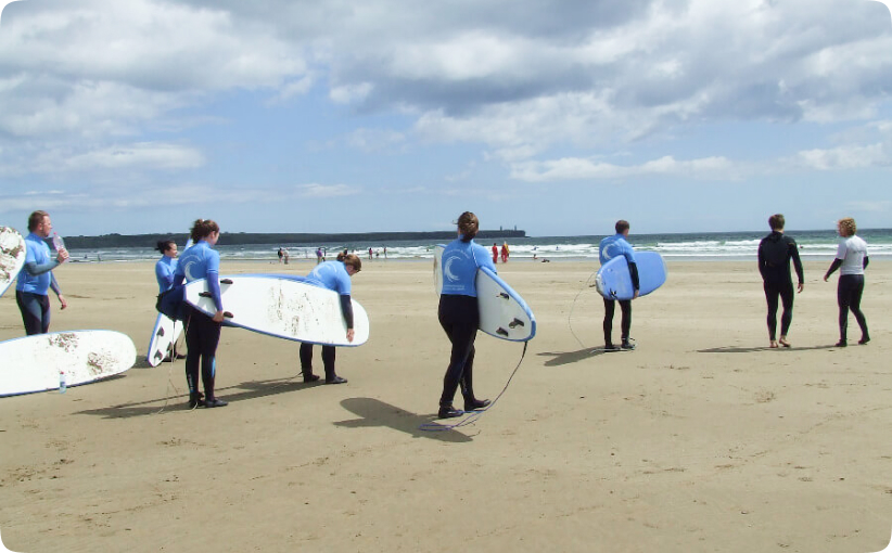 Group of surfers carrying boards across the beach toward the shoreline during a lesson.