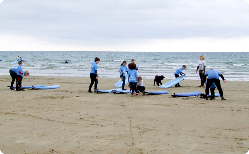 Children and instructor preparing surfboards on the beach before entering the water for a lesson.