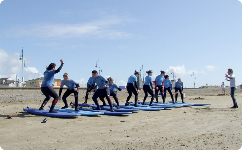 Group of surfers practicing pop-up technique on boards on the sand while an instructor watches.