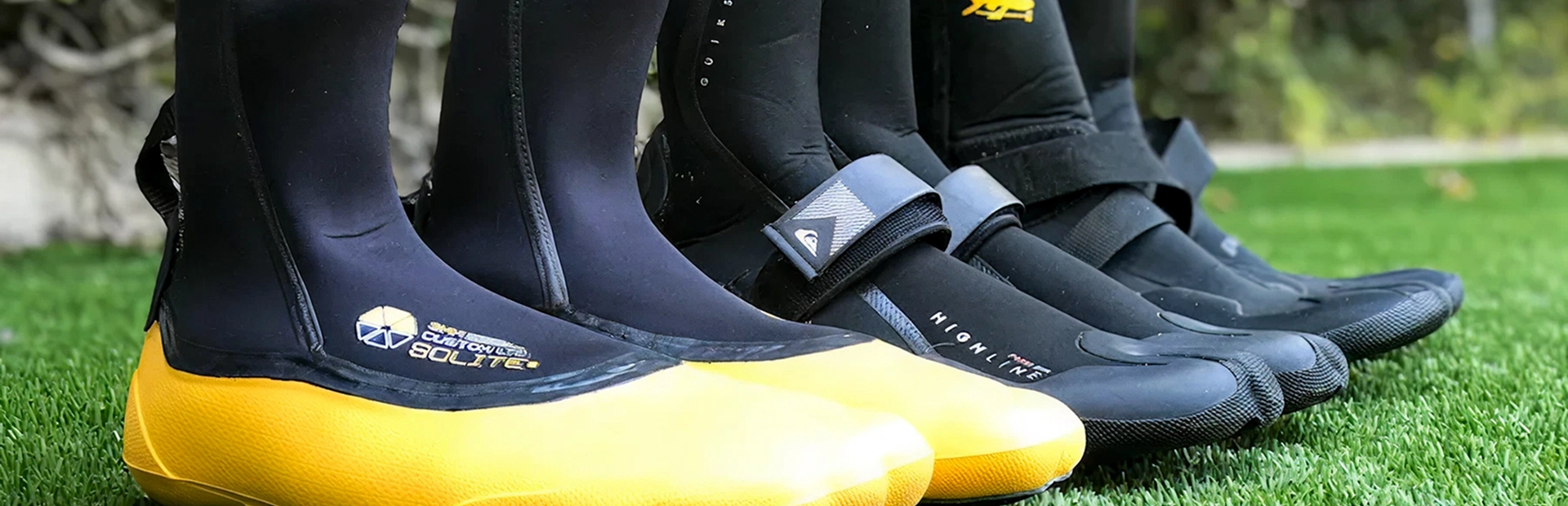 Neoprene water sports boots lined up on grass, including yellow-soled and black surf booties.