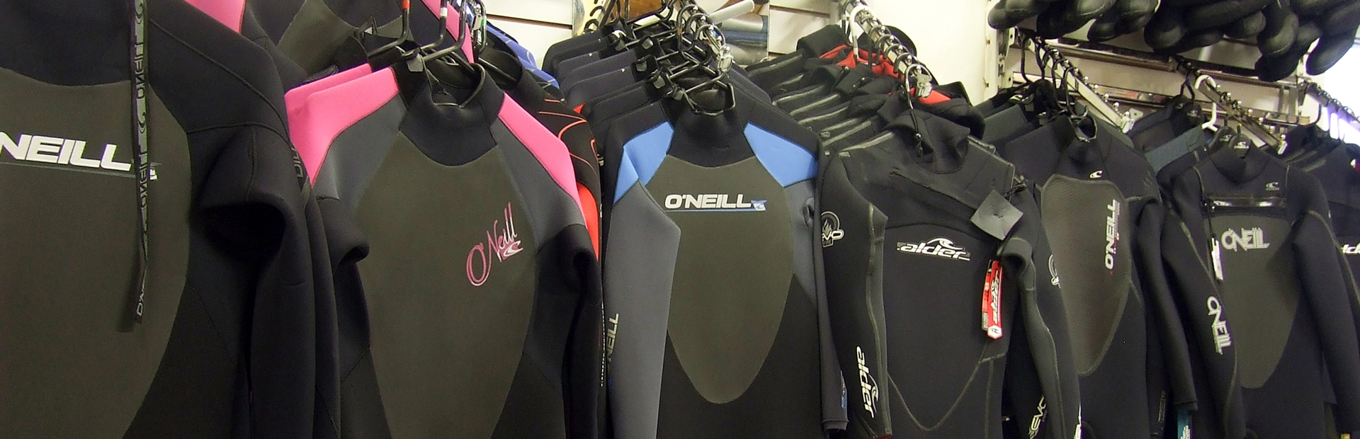Selection of wetsuits hanging on racks inside a surf equipment shop.