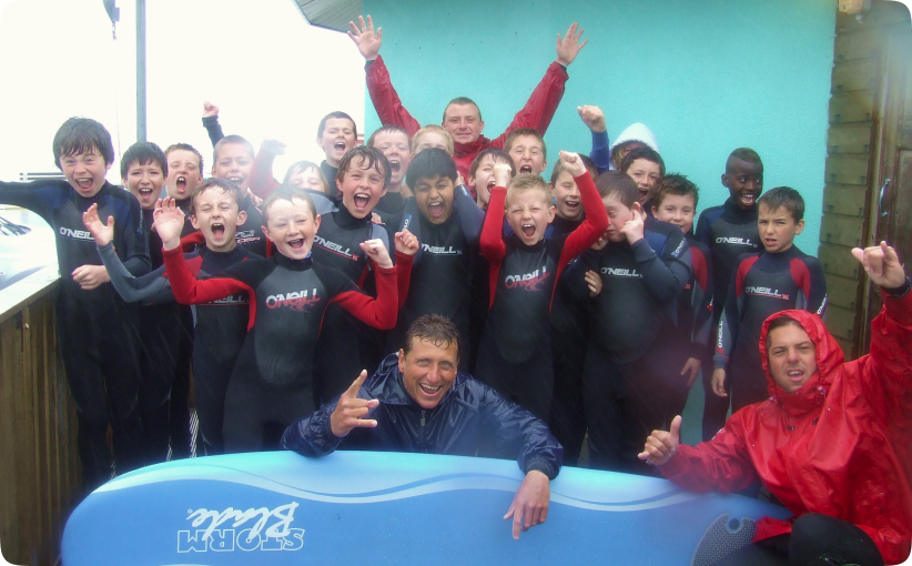 Group of children in wetsuits cheering together with instructors after a surf lesson.