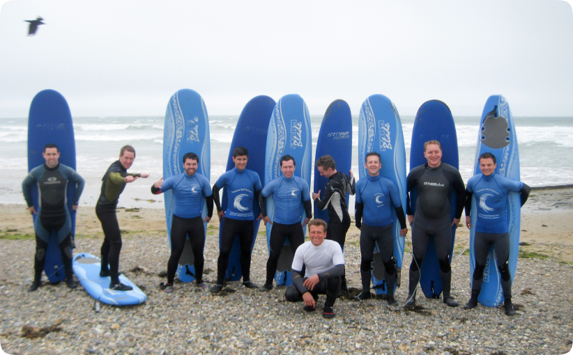 A stag party group in wetsuits posing on the beach with surfboards, smiling and celebrating before or after their surf session by the sea.