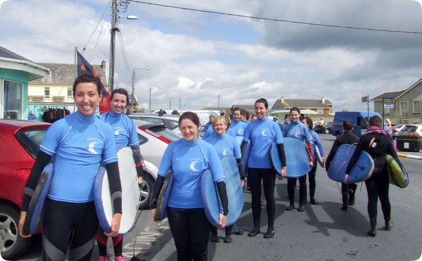 A hen party group in wetsuits walking together with surfboards, smiling and heading toward the beach for their surf lesson, capturing a fun and energetic pre-surf moment.