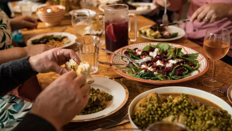 People sharing a meal at a table with plates of salad and various dishes, drinks, and bread.