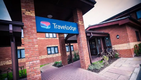 Entrance to a Travelodge hotel with a blue sign above the doorway and brick exterior.