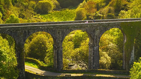 Waterford Bridge Stone railway viaduct with multiple arches spanning a green valley with trees and a path below.