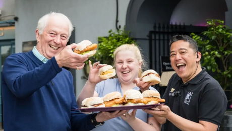 Three people smiling and holding a tray of sandwiches during a food tour.
