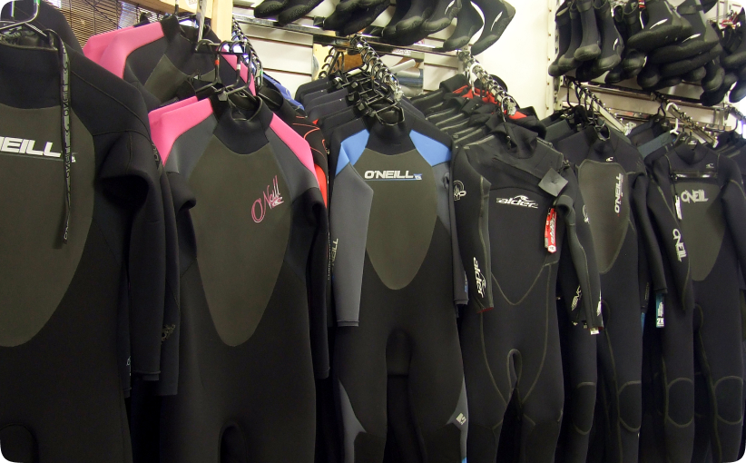Selection of wetsuits hanging on racks inside a surf equipment shop.