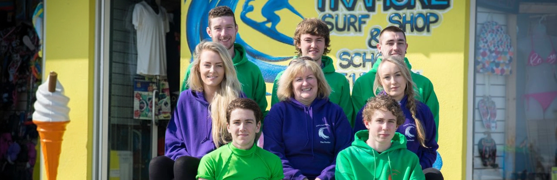 Surf school team posing outside a surf shop wearing branded hoodies.